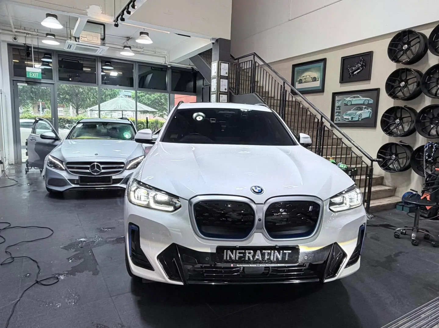 A white BMW X5 SUV facing the camera with a Mercedes-Benz sedan behind it.