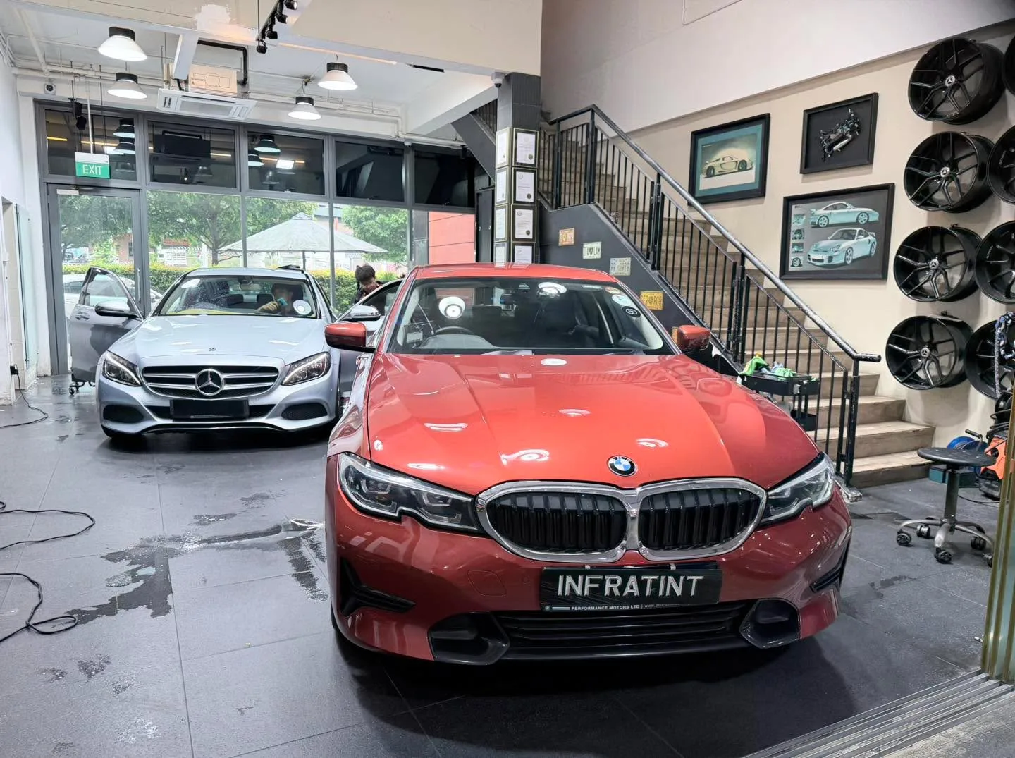 A red BMW sedan facing forward with a silver Mercedes-Benz sedan in the background.