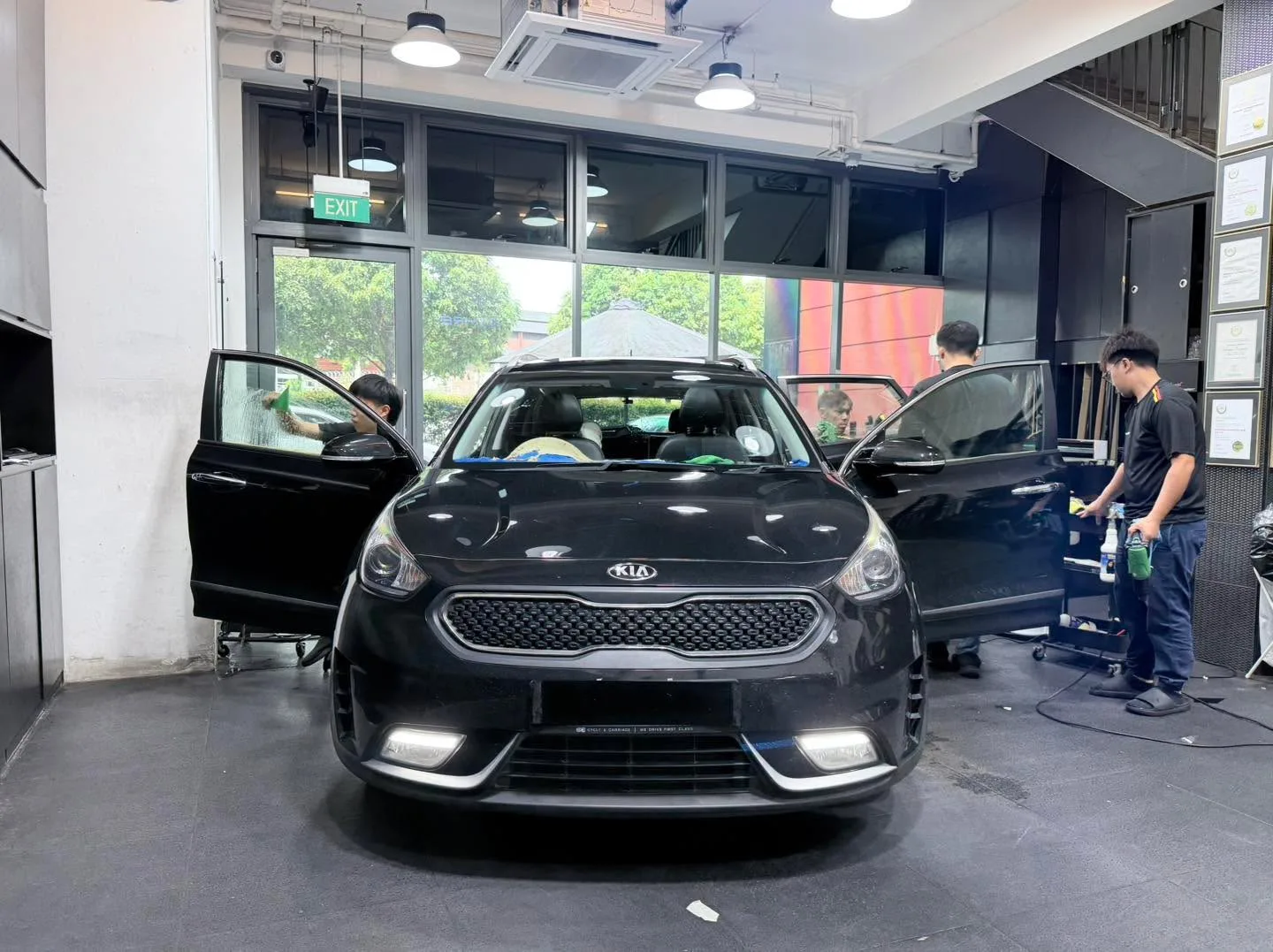 A black Kia hatchback with doors open, staff working on tinting the windows.