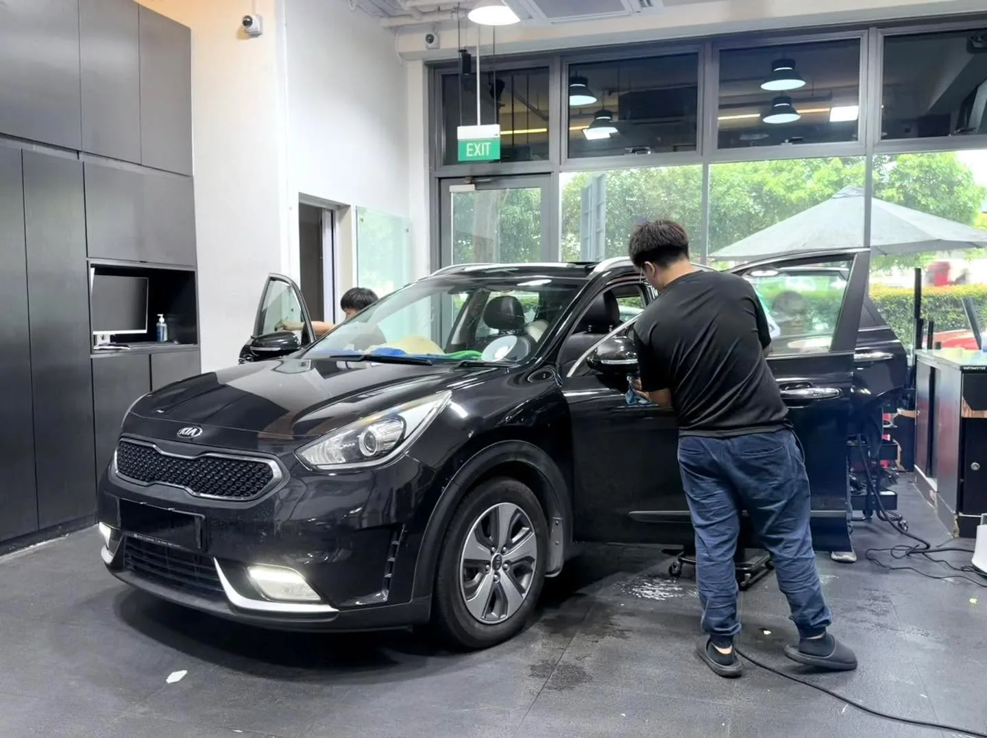 A black Kia hatchback with open door and staff applying window tint.