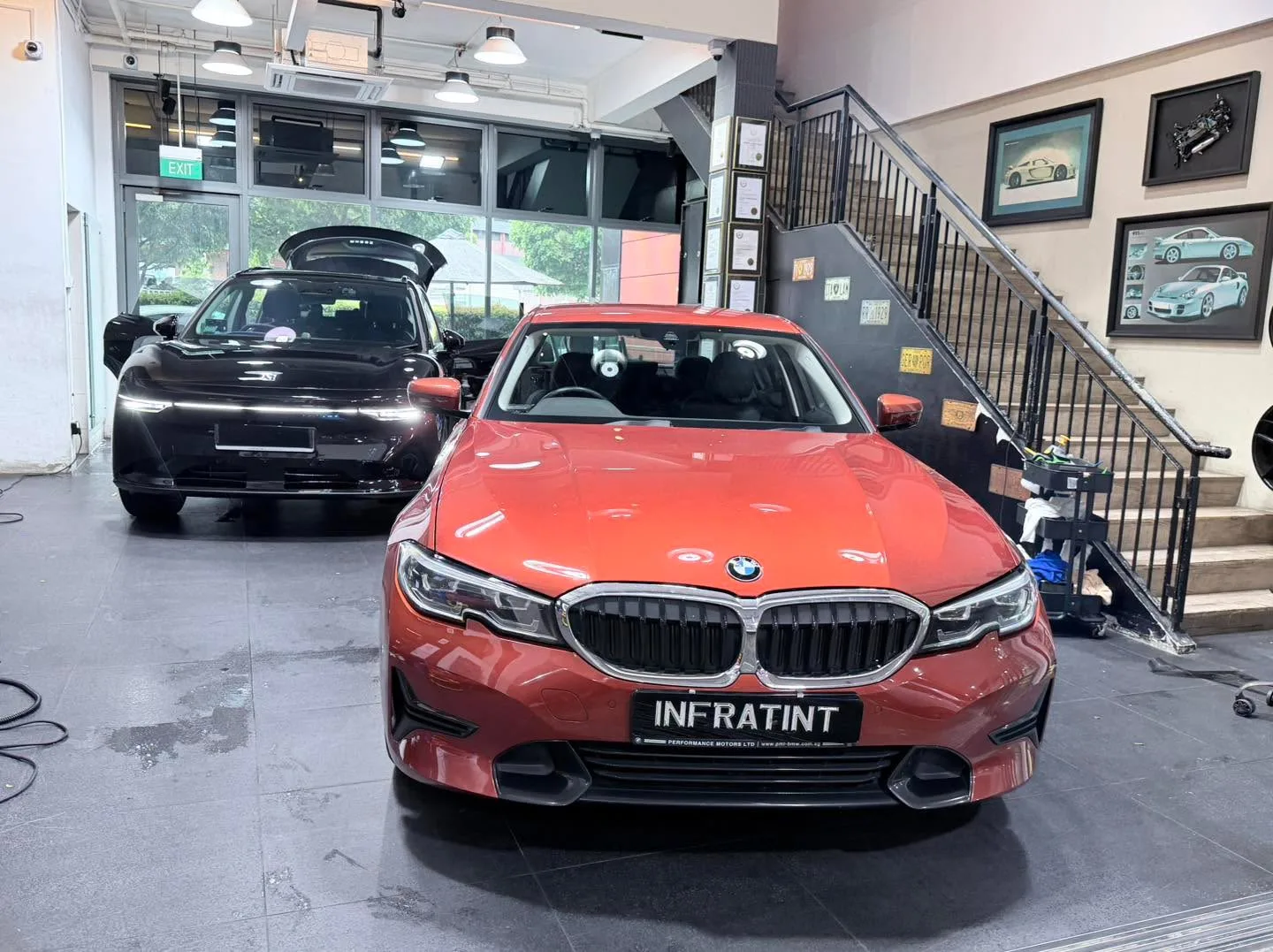 A red BMW sedan and black hatchback parked side by side in the workshop.