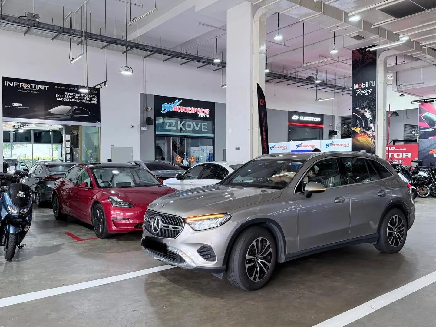 A silver Mercedes-Benz SUV and red Tesla sedan in the workshop among other vehicles.