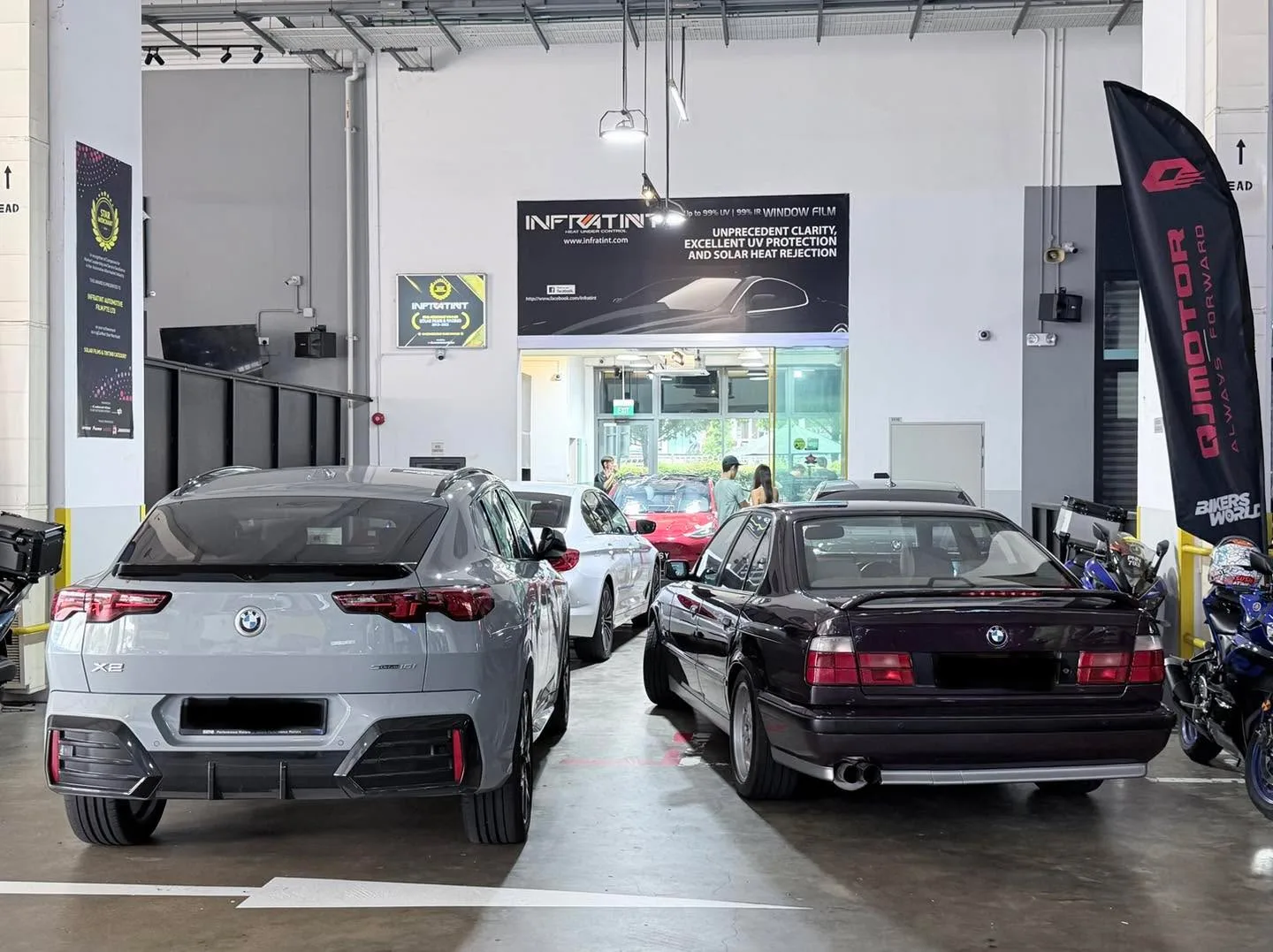 A white BMW sedan, a white and red Tesla, and a black BMW in the workshop interior.