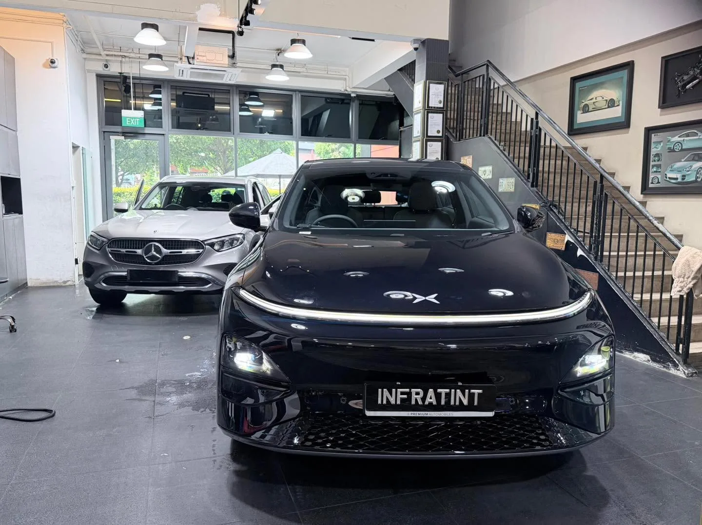 A black XPENG sedan facing the camera in the workshop with a silver Mercedes-Benz SUV behind.