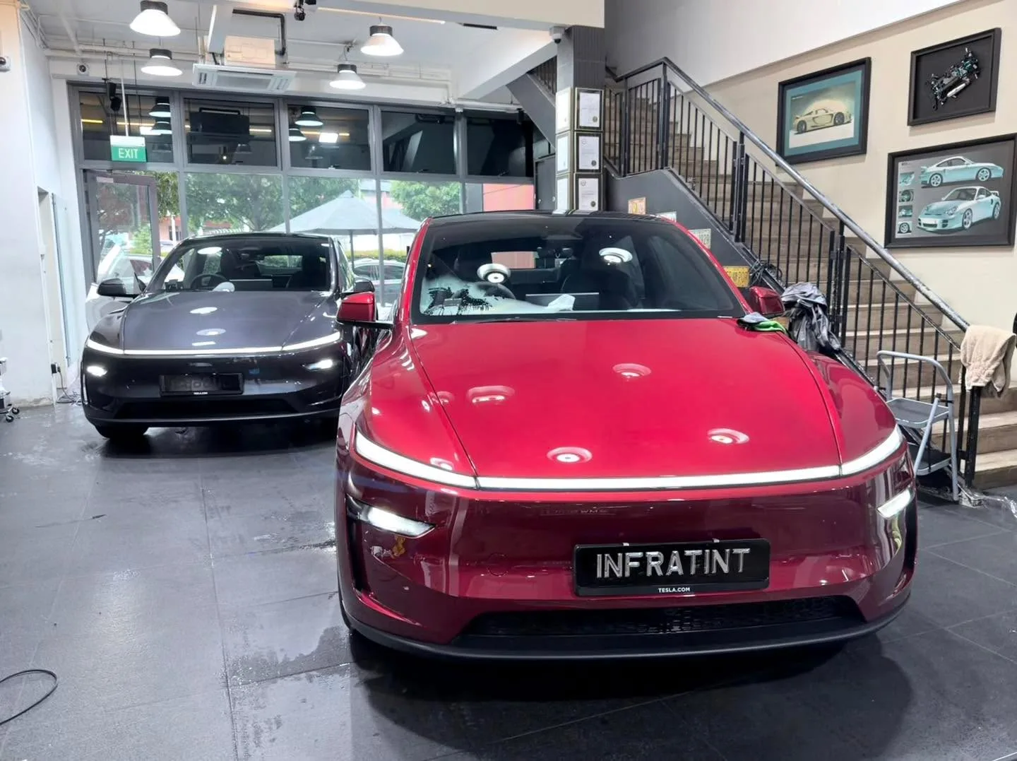 A red Tesla sedan and dark-coloured car beside it in the workshop.