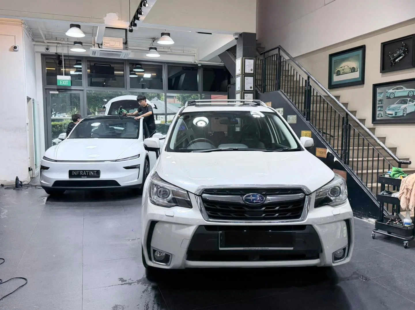 A white Subaru Forester and white Tesla Model Y sedan in the workshop with technicians working.