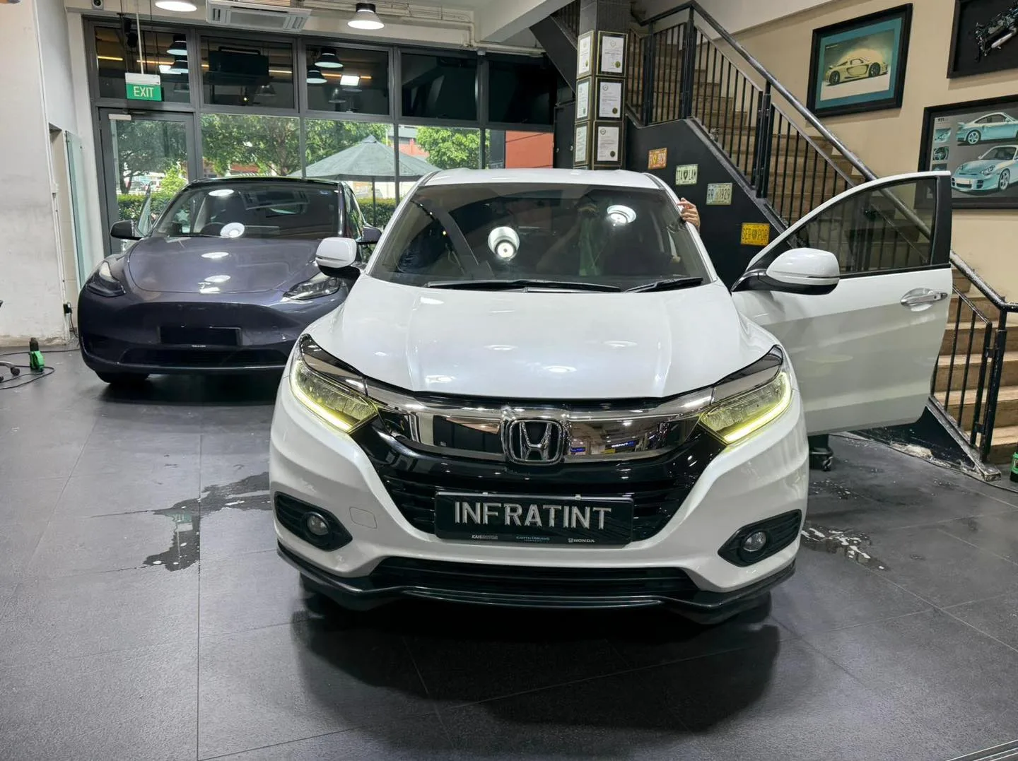 A white Honda Vezel with door open, a dark grey Tesla in the background, and a white car on the right.
