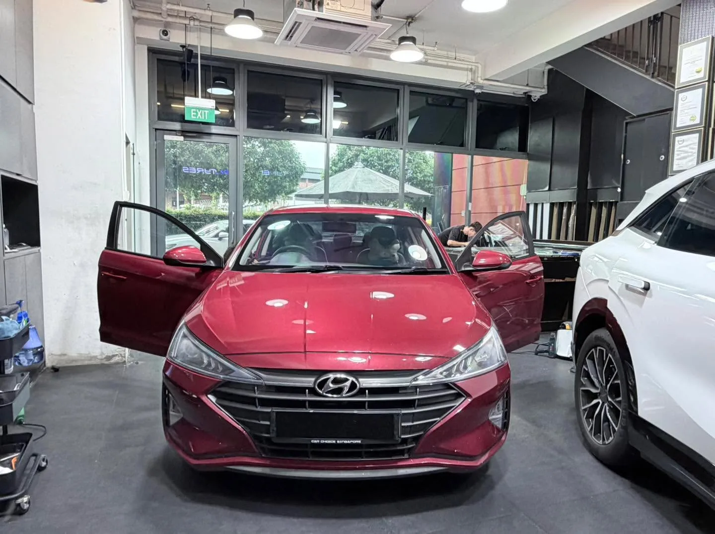 Red Hyundai Avante sedan with doors open, with a white vehicle visible behind it.