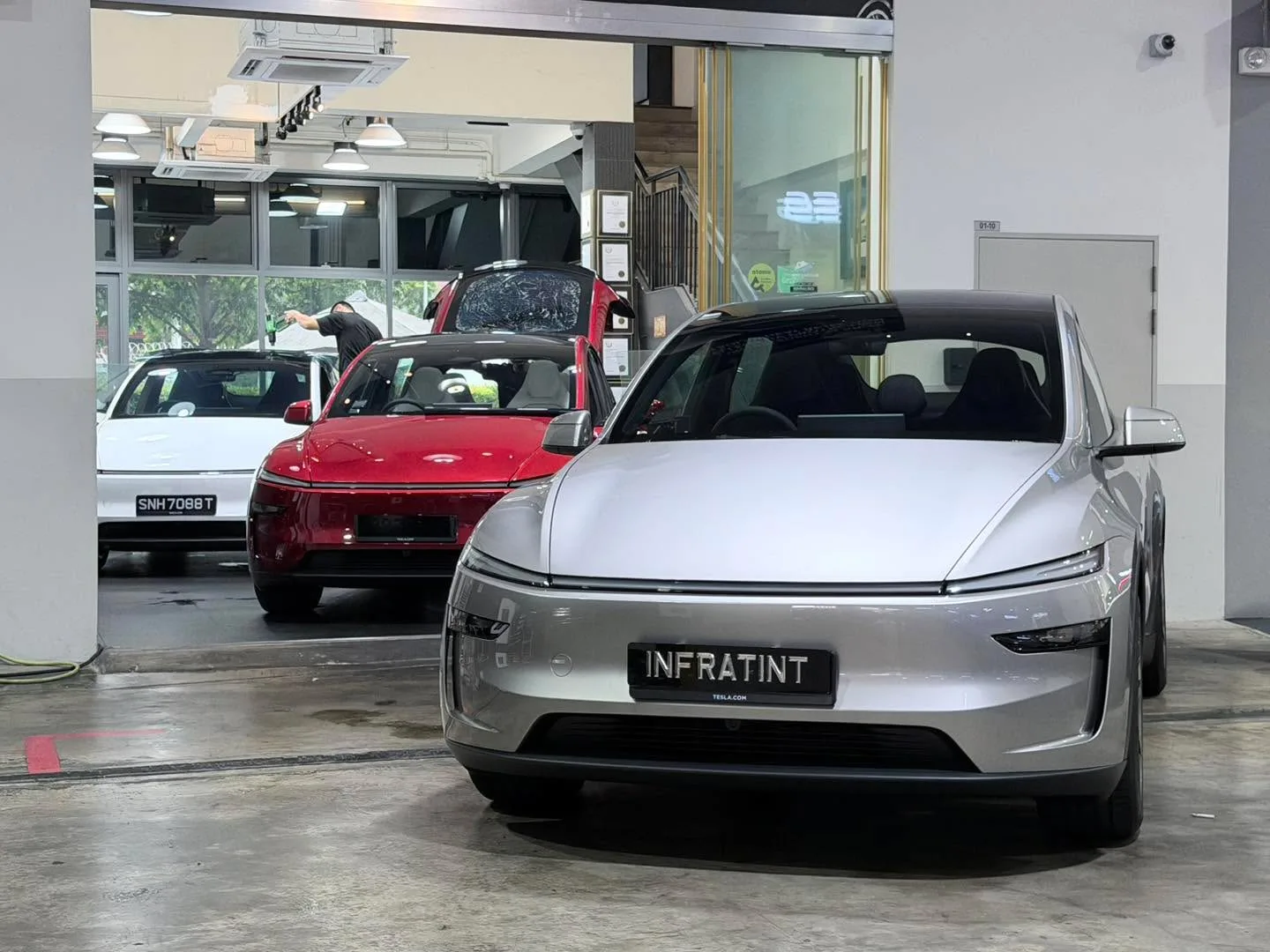 A silver Tesla sedan and a red Tesla sedan parked in the Infratint workshop.