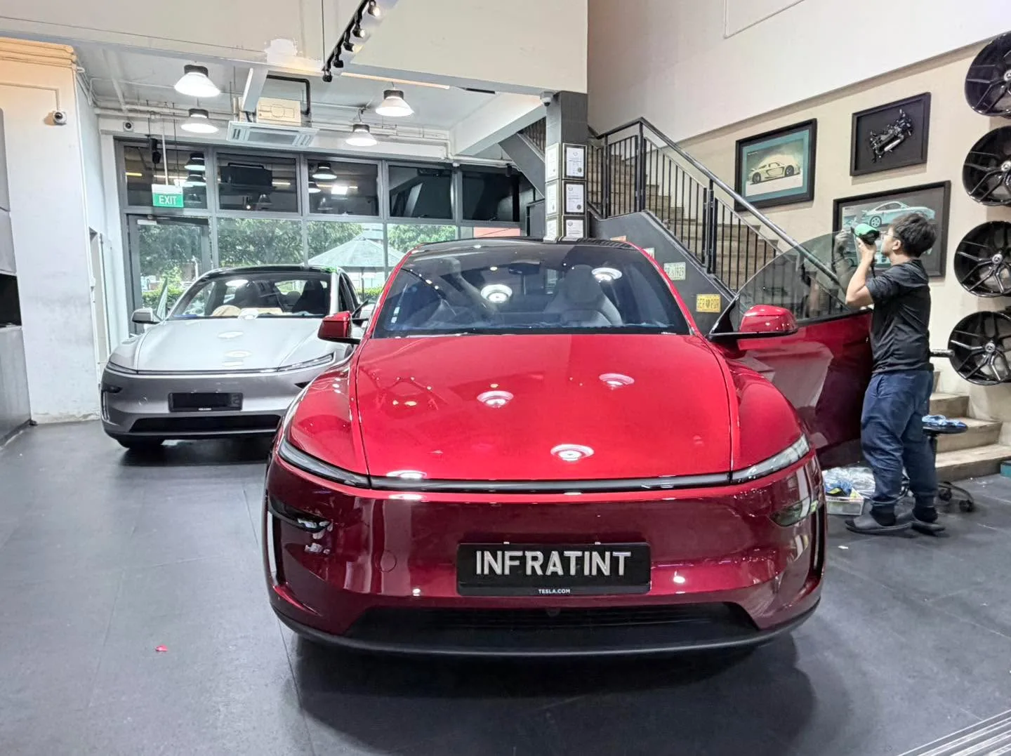 A red Tesla sedan with open door in the workshop, with a silver sedan visible behind.