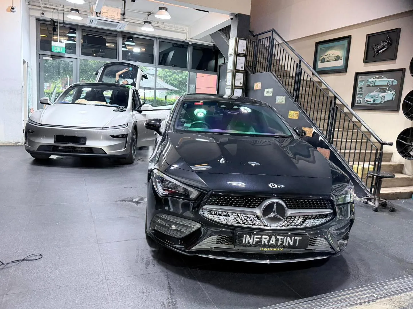 A black Mercedes-Benz sedan and a silver Tesla sedan in the workshop.