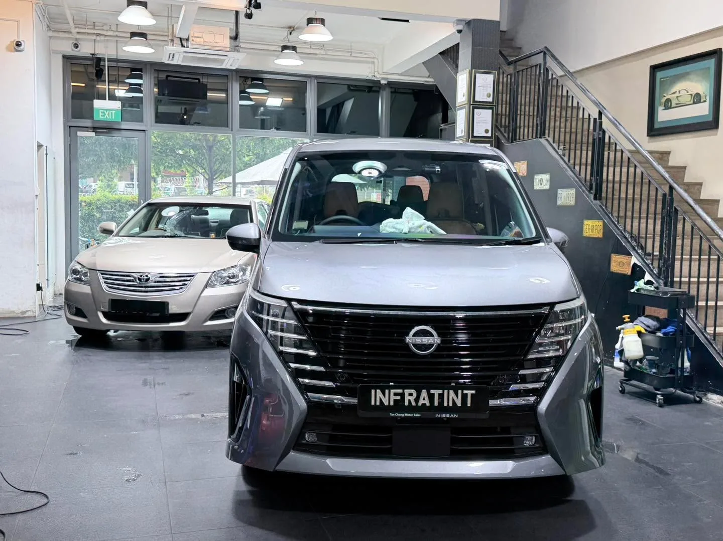 A grey Nissan minivan with a white Peugeot visible in the workshop.