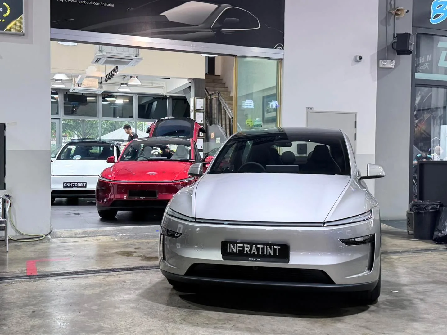 A silver Tesla Model Y is parked indoors at Infratint, with a red Tesla visible behind it.