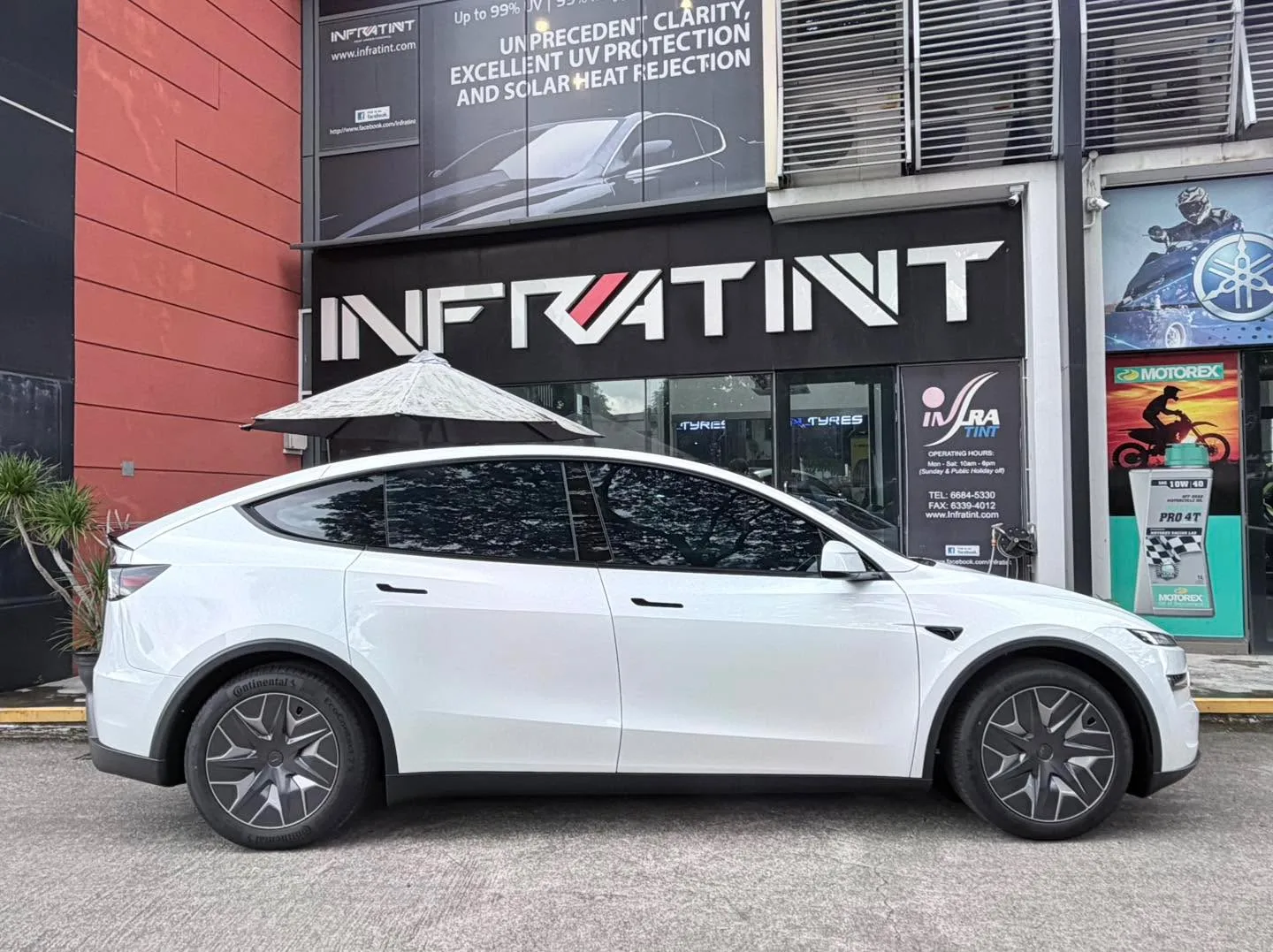 A white Tesla Model Y is parked outside the Infratint storefront under a shade.
