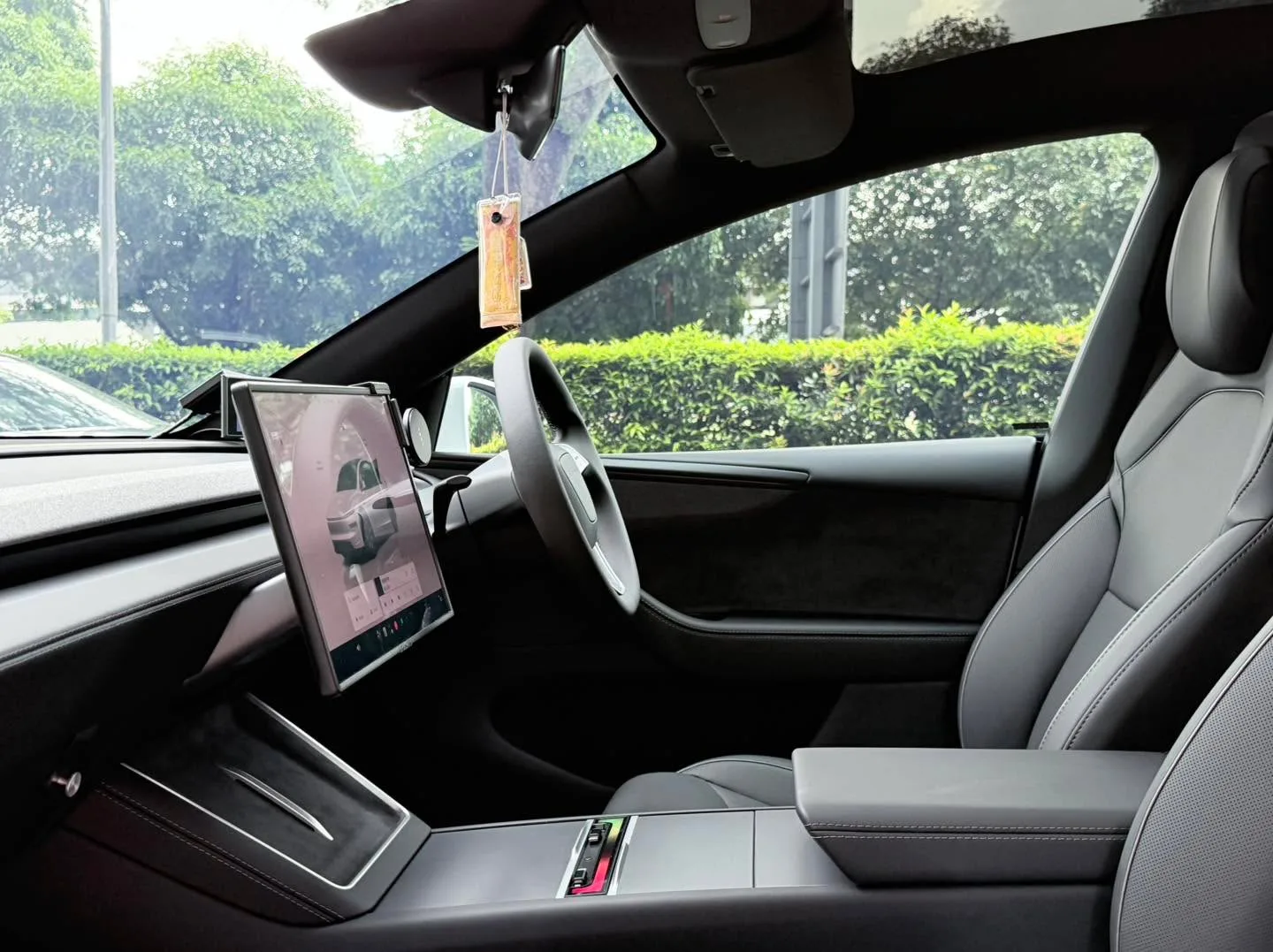The interior of a Tesla Model Y showing the steering wheel, centre touchscreen, and windscreen tinting.