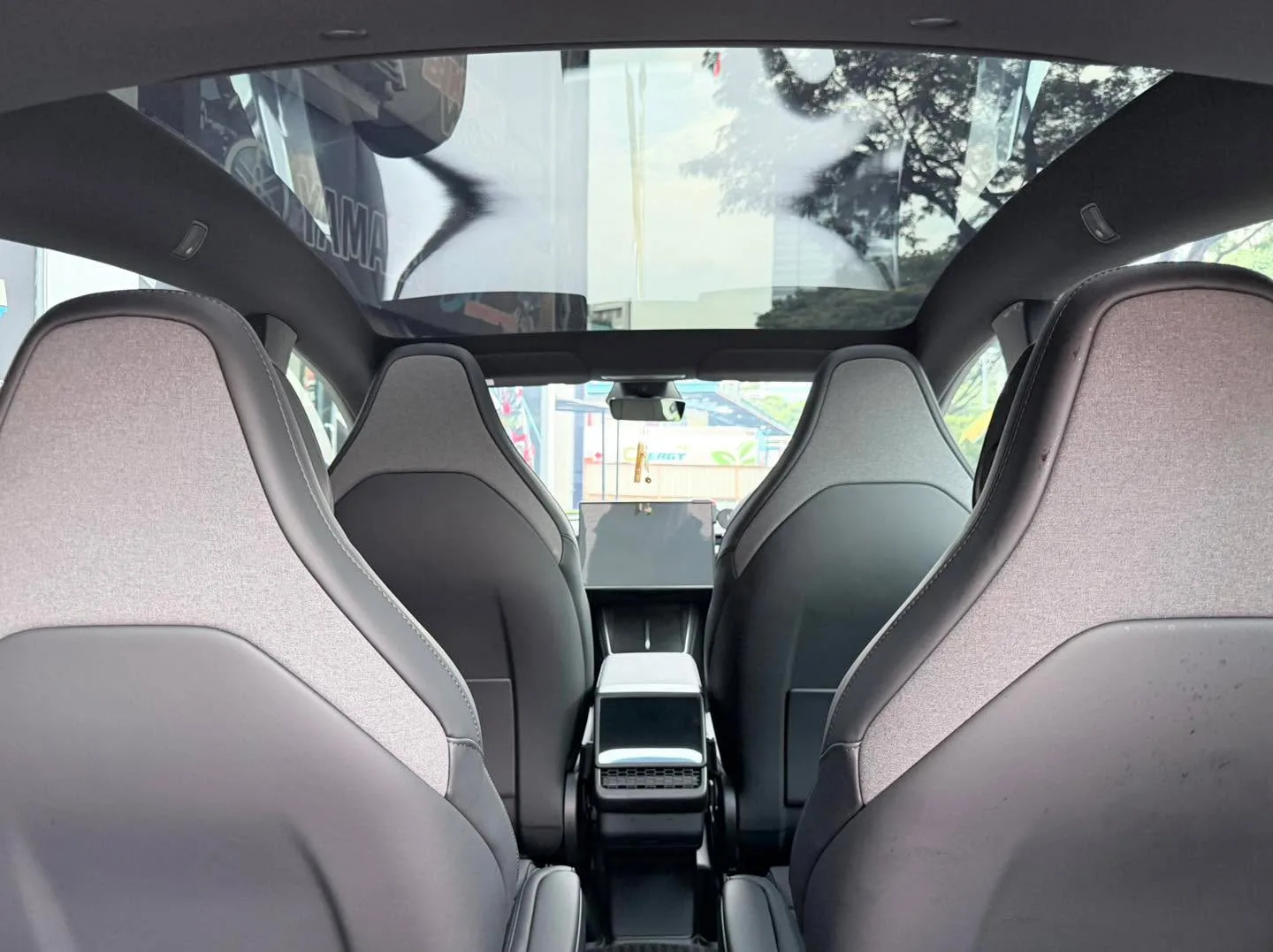 The interior of a Tesla Model Y viewed from the rear seats, showing the panoramic roof with tinting applied.