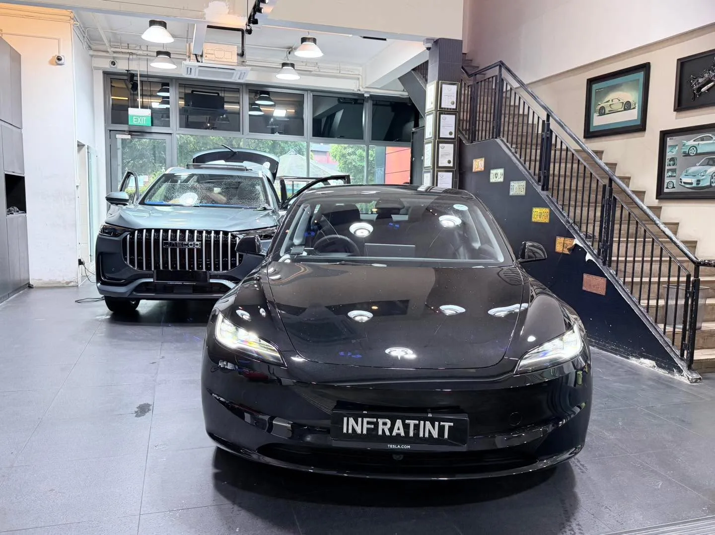 A black electric sedan and a dark SUV parked indoors under workshop lights.