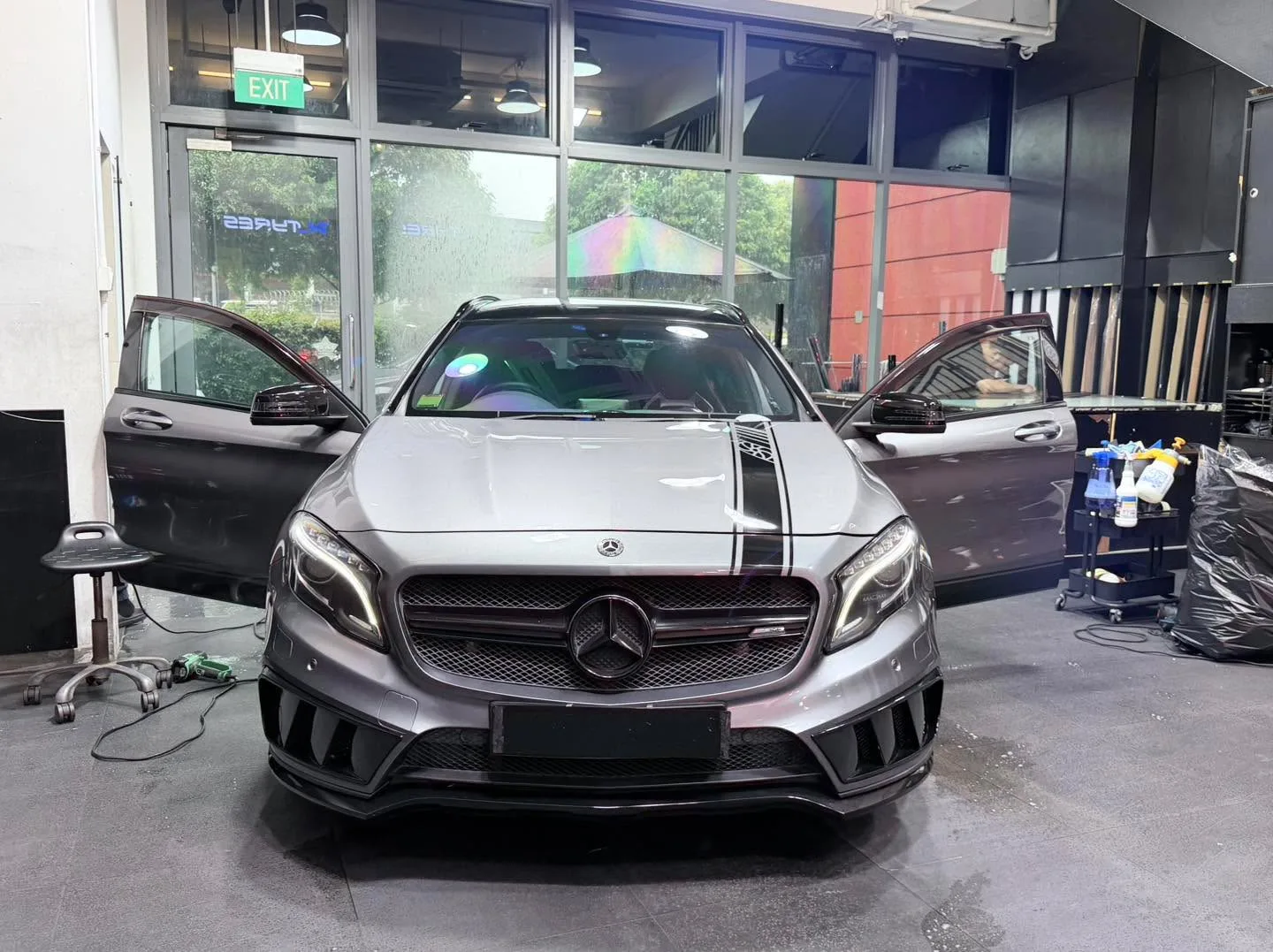 A dark saloon car with distinctive grille viewed head-on inside the workshop.
