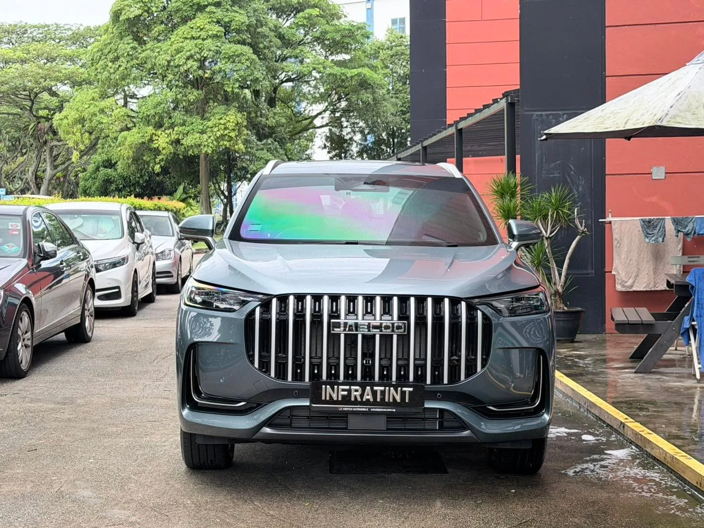 A grey Jaecoo J8 SUV parked outside Infratint, viewed from the front.