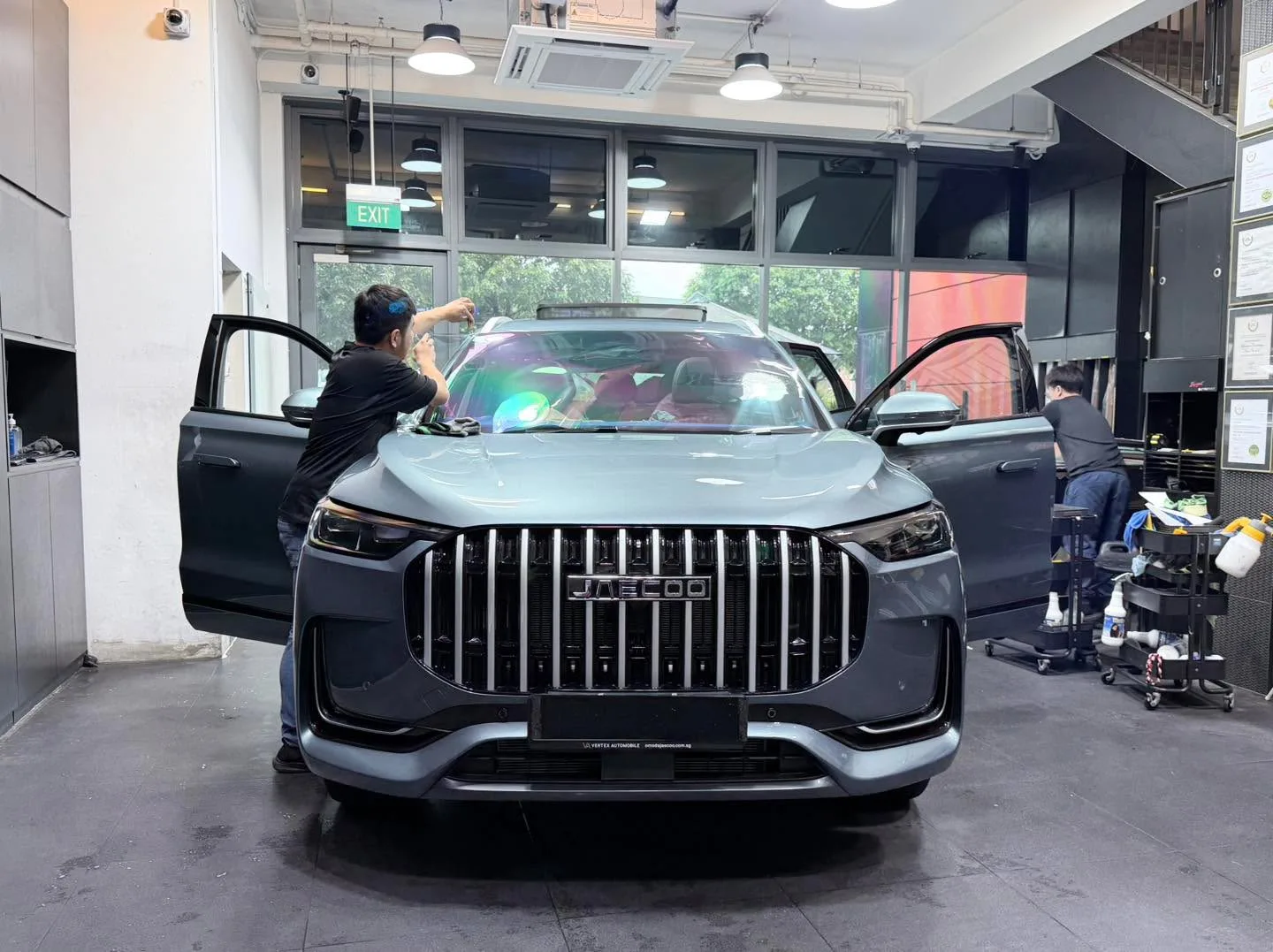 A grey Jaecoo J8 with doors open inside the Infratint workshop, technicians working on the windows.