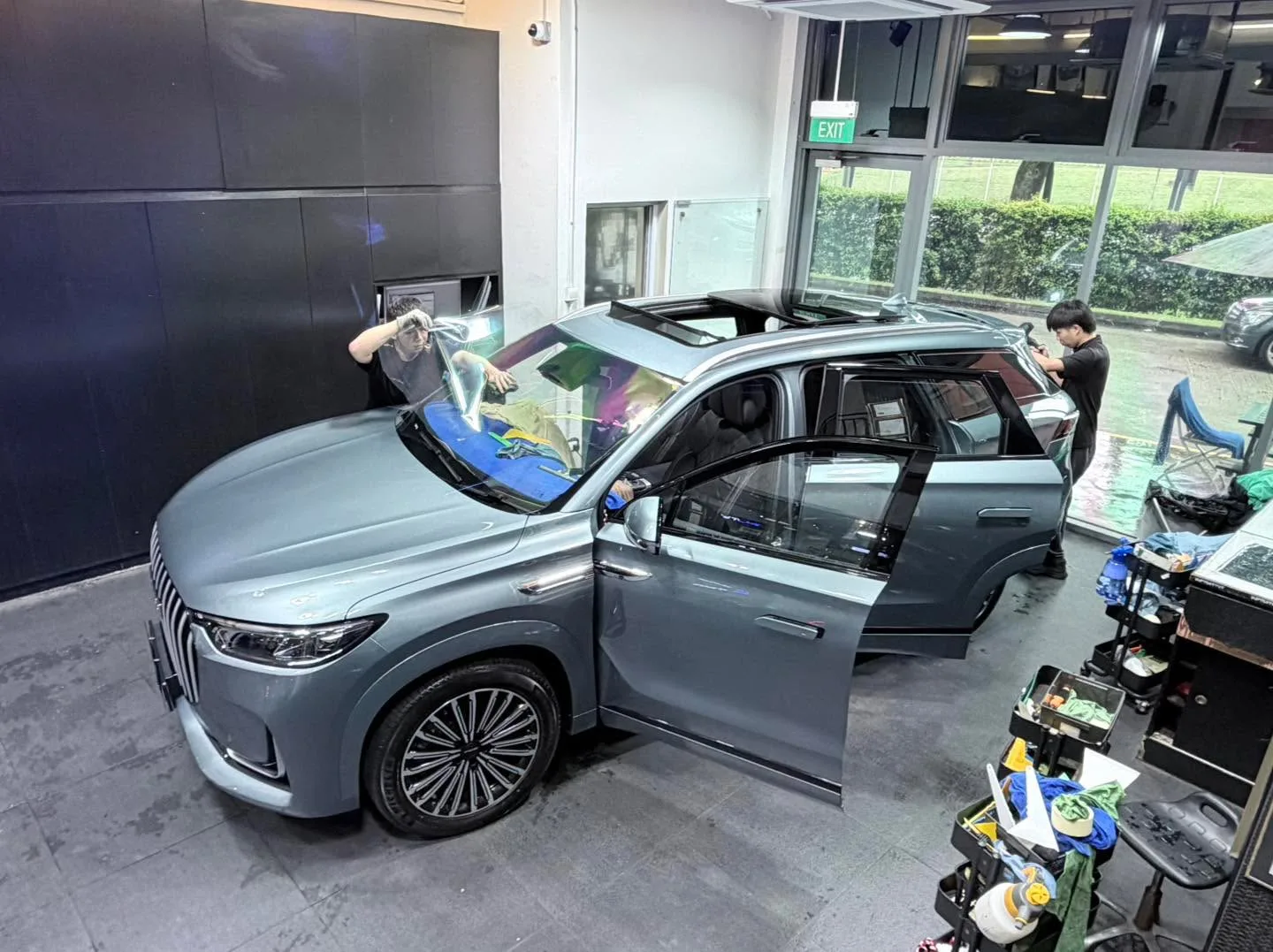 Front-facing view of the grey Jaecoo J8 with doors open, technicians working on the windows.