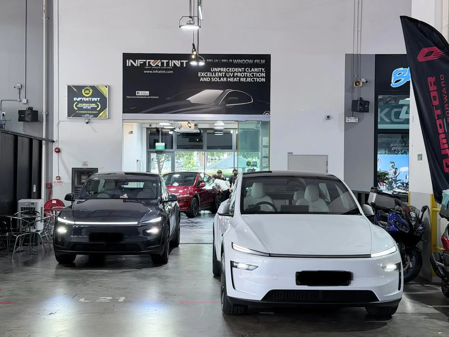 A white Tesla Model Y and a black Tesla Model Y parked inside the workshop.