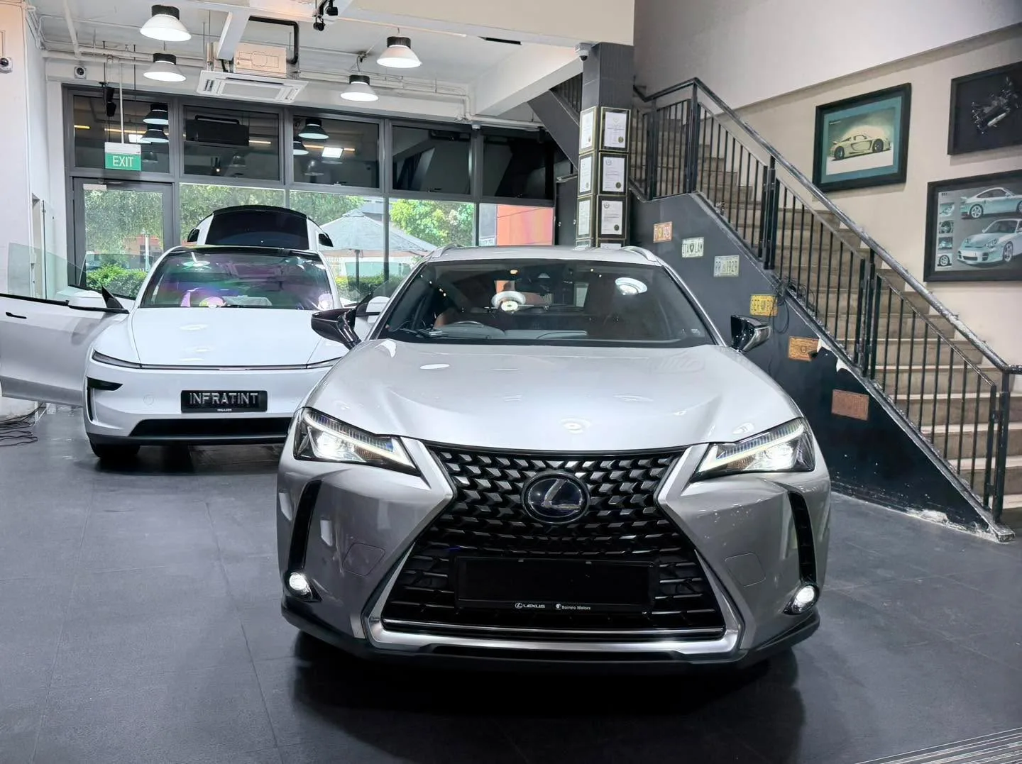 A white Tesla Model Y and a grey Lexus UX compact SUV parked inside the workshop.