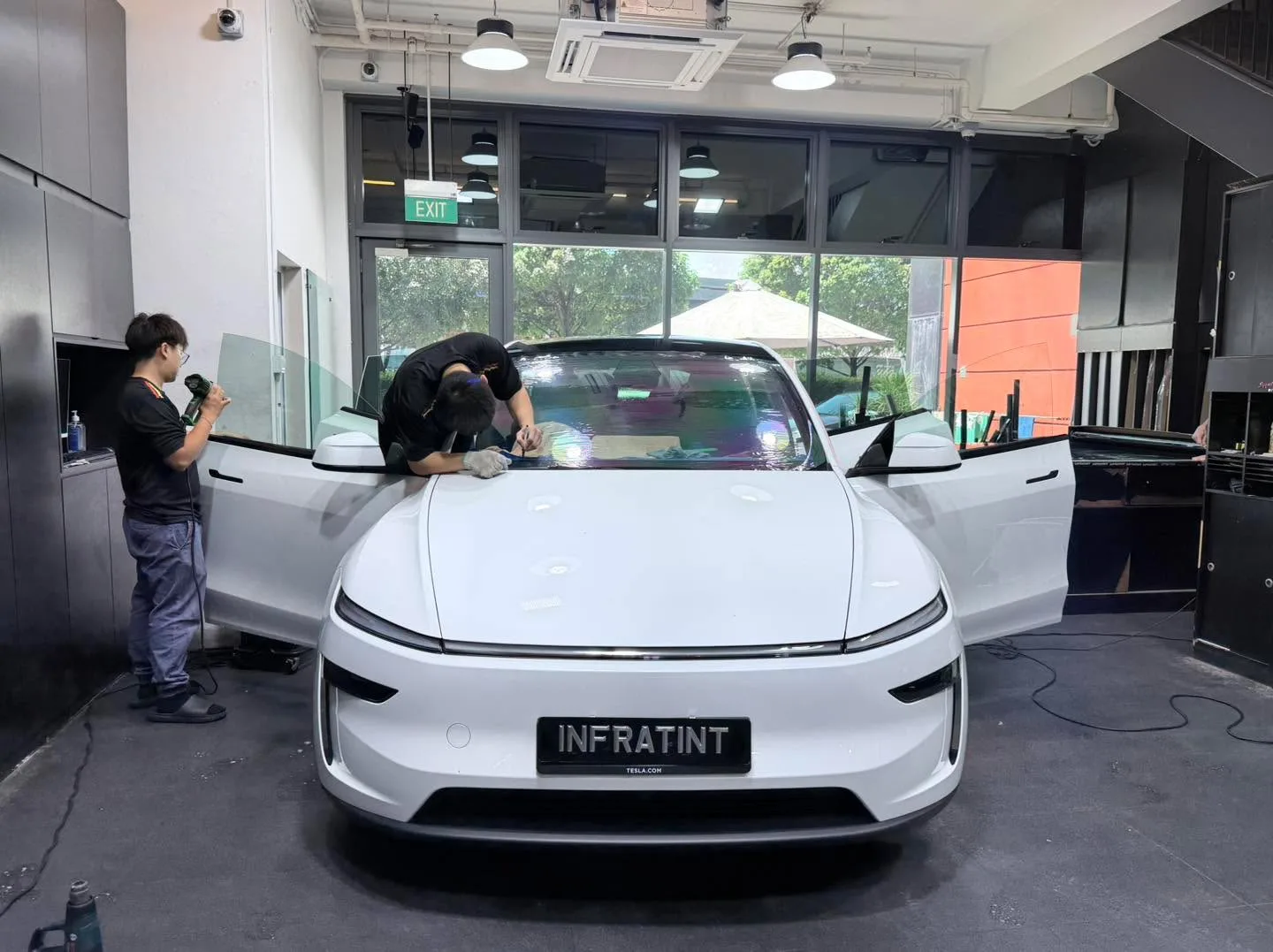 A white Tesla Model Y sedan with doors open, technicians working on the vehicle.