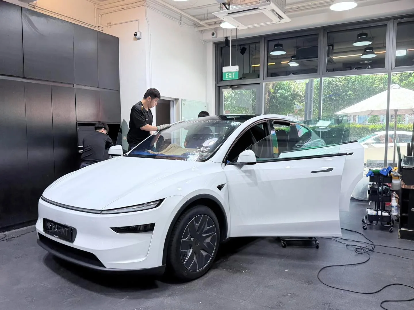 A white Tesla Model Y SUV with a door open during the tinting process.