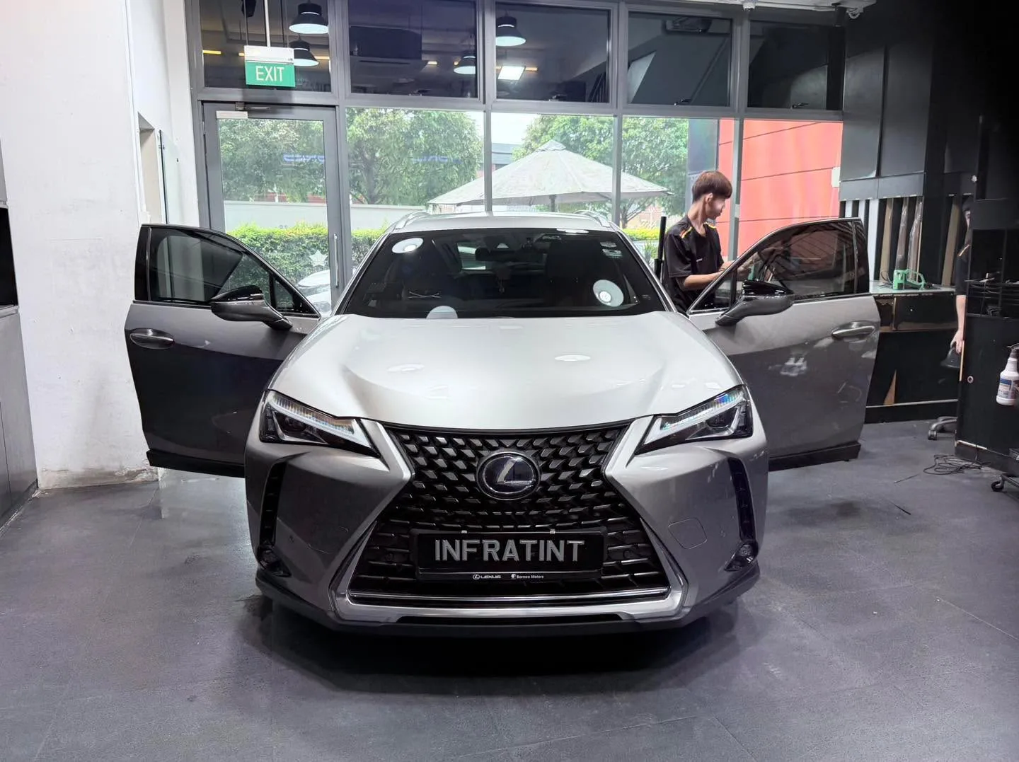 A grey Lexus UX with both doors open, technician applying film to the windows.