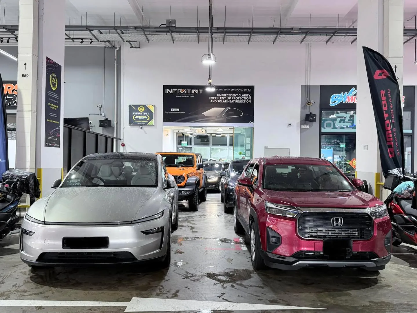 A silver Tesla sedan and a maroon Honda SUV parked side by side in the workshop.