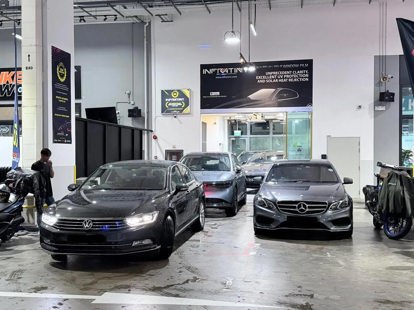 A black Volkswagen sedan, a silver Tesla sedan, and a black Mercedes-Benz sedan parked in the workshop.