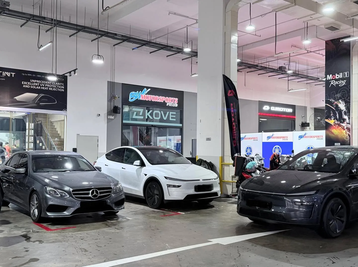 A grey Mercedes-Benz sedan, a white Tesla sedan, and a dark Tesla sedan in the workshop.