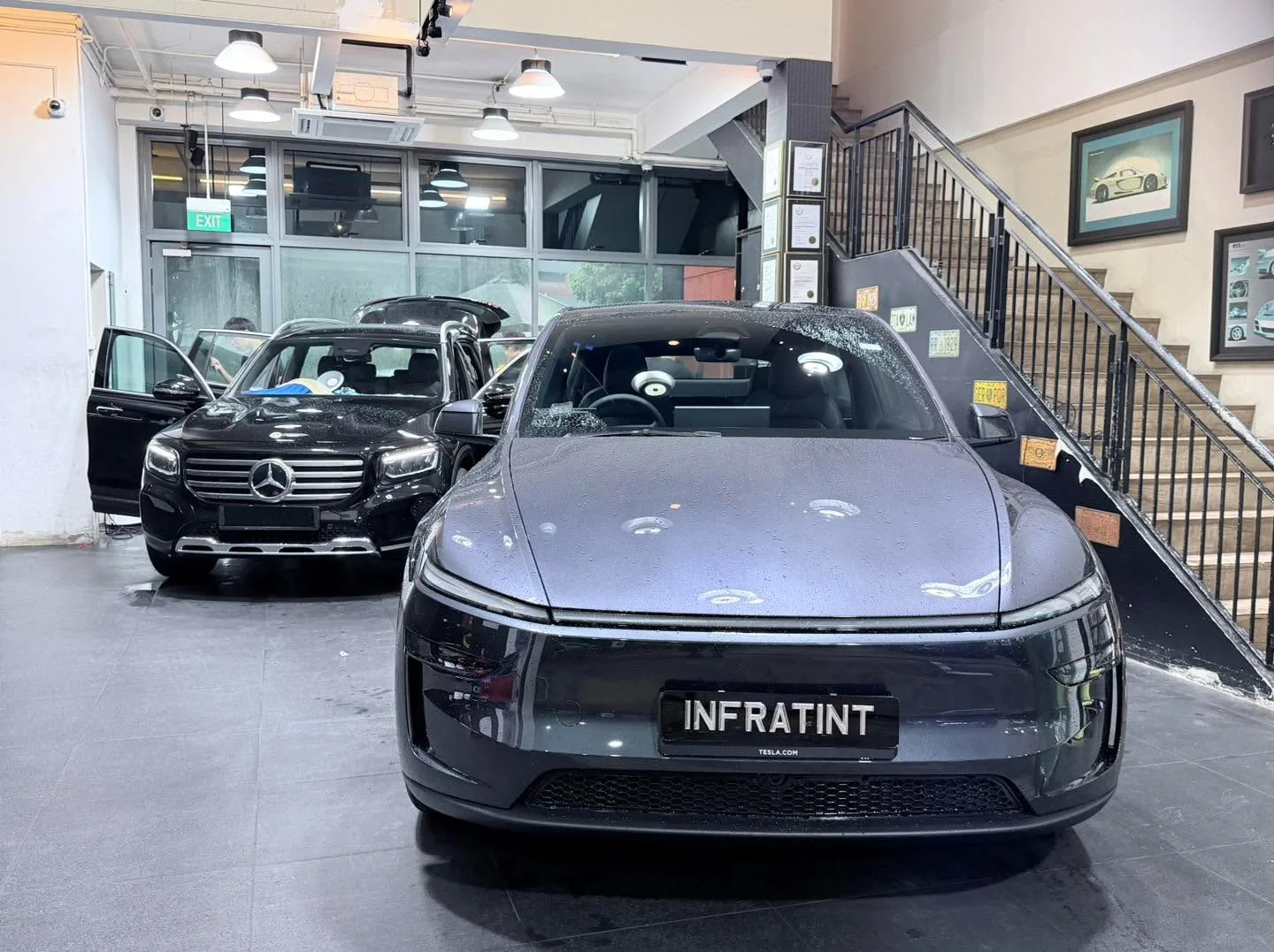 A grey Tesla sedan and a maroon Honda SUV with doors open, parked indoors.