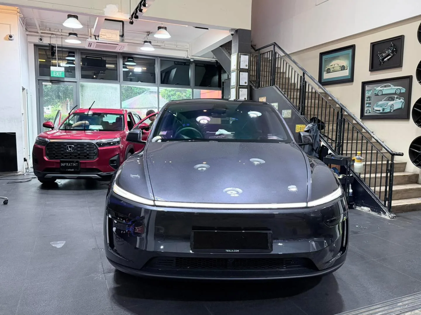 A dark Tesla sedan and a maroon Honda SUV parked in the workshop.