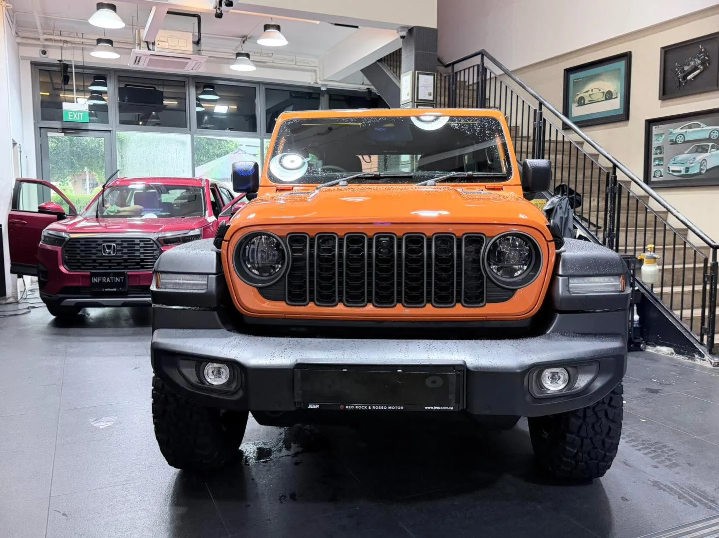 An orange Jeep Wrangler and a white Tesla sedan parked indoors.