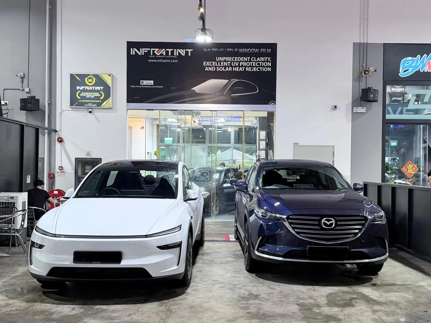 A white Tesla and a dark blue Mazda CX-9 parked outside the Infratint workshop.