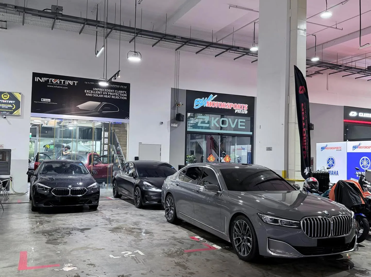 A black BMW, a black Tesla, and a silver BMW sedan parked indoors at a garage facility.