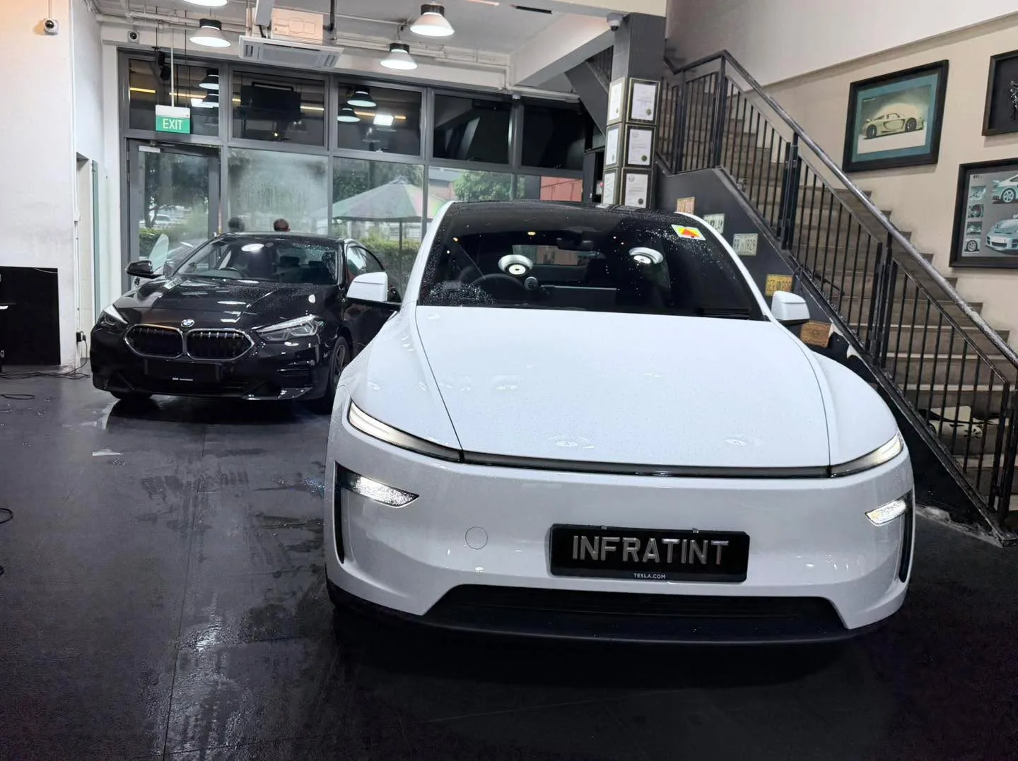 A white Tesla sedan and a black BMW sedan facing the camera inside the workshop.
