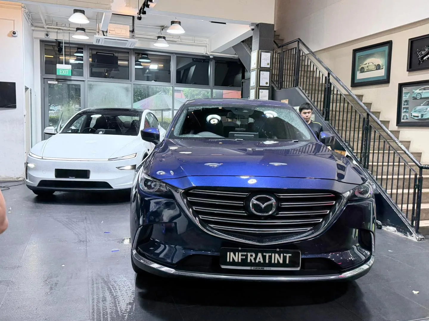A white Tesla sedan and a dark blue Mazda CX-9 indoors at the workshop.