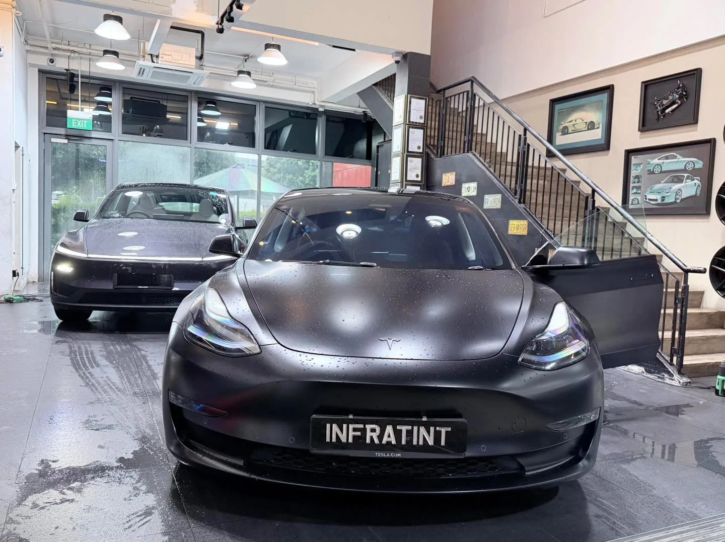 A black Tesla sedan wet with water droplets and two other vehicles behind it.