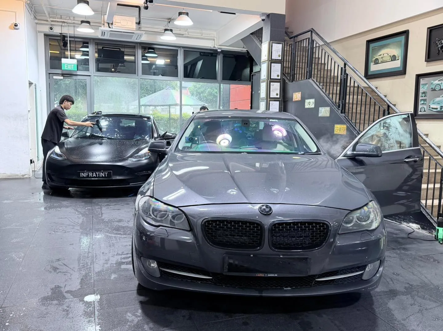 A black Mercedes-Benz SUV and a black Tesla sedan indoors, with a technician working.