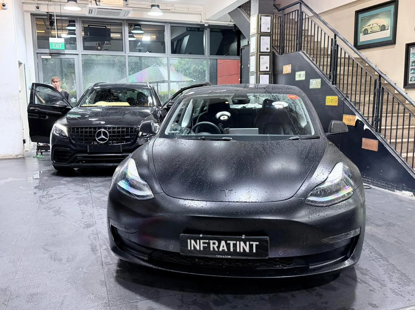 A grey BMW sedan and a black BMW sedan indoors at the workshop.