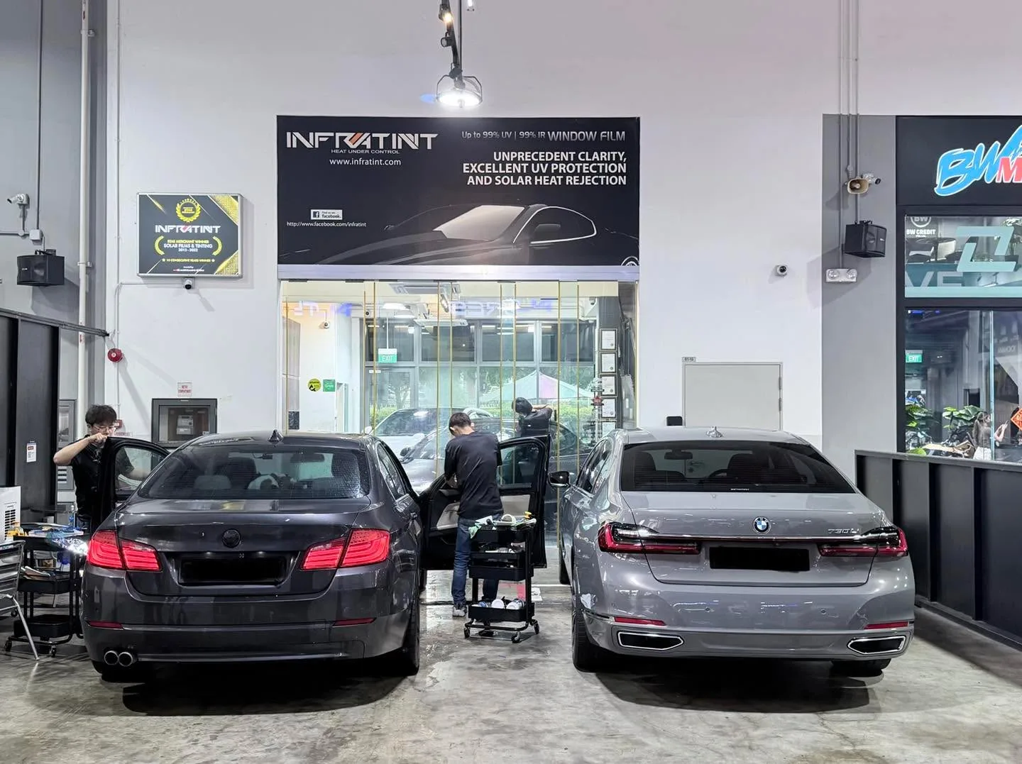 Two BMW sedans parked outside the workshop, viewed from the rear.