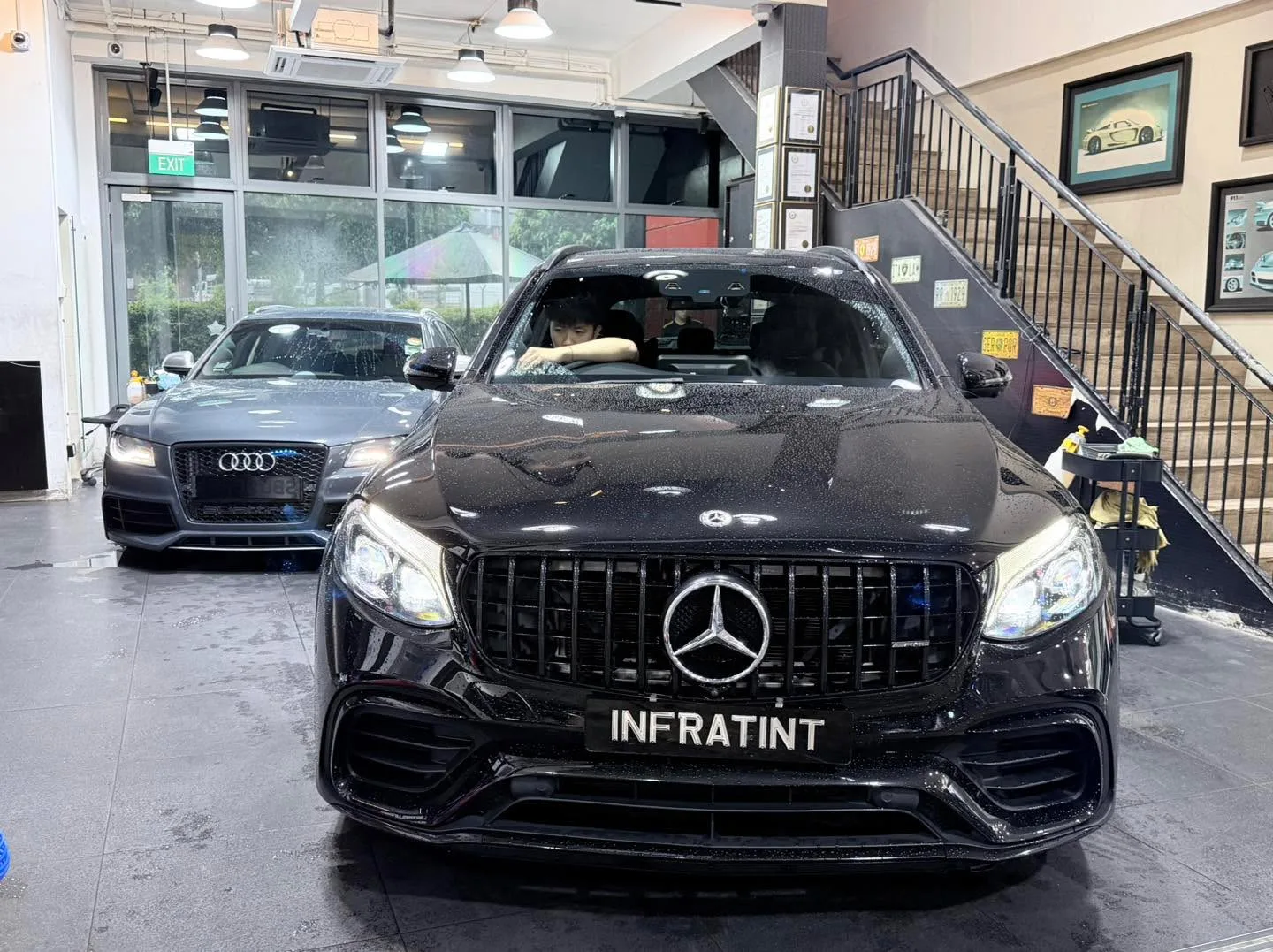 A black Mercedes-Benz SUV in the foreground and an Audi sedan behind it inside the workshop.