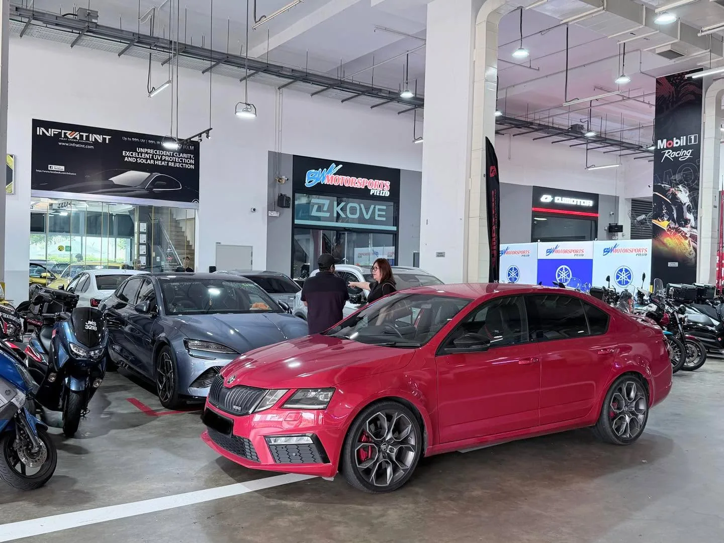 A red saloon and a grey saloon parked in a workshop with exposed ceiling and signage.