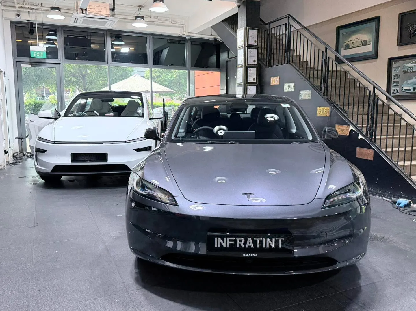 A grey Tesla sedan and a white Tesla sedan parked indoors.