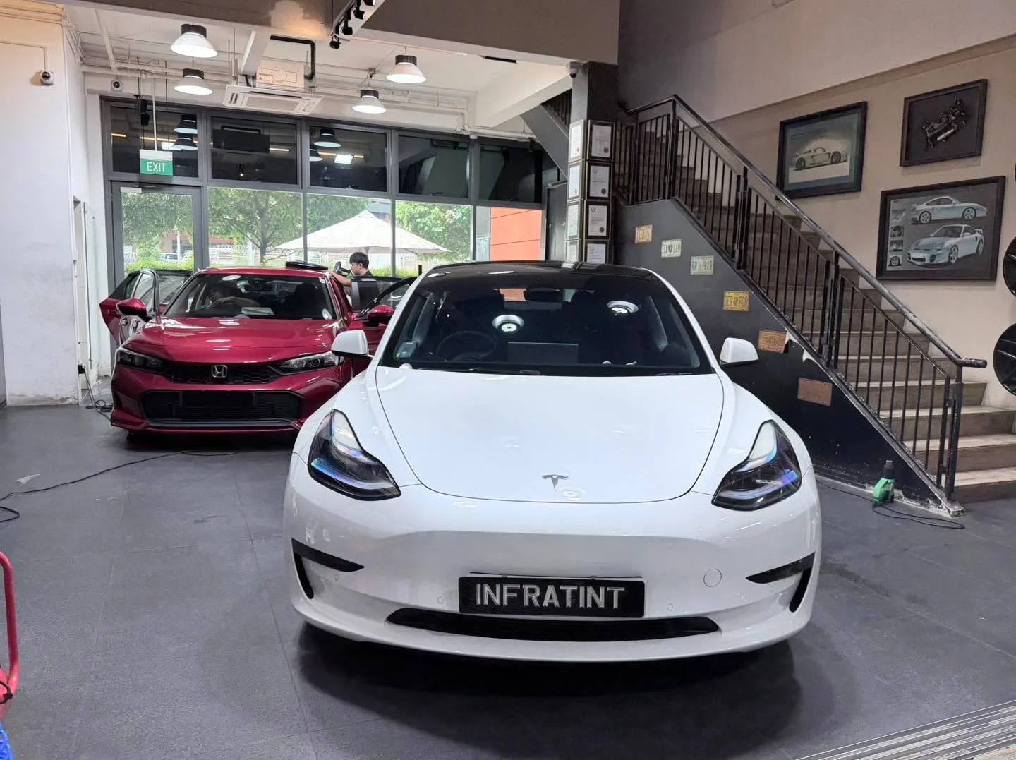 A white Tesla Model Y and red Honda Civic parked indoors with a technician between them.