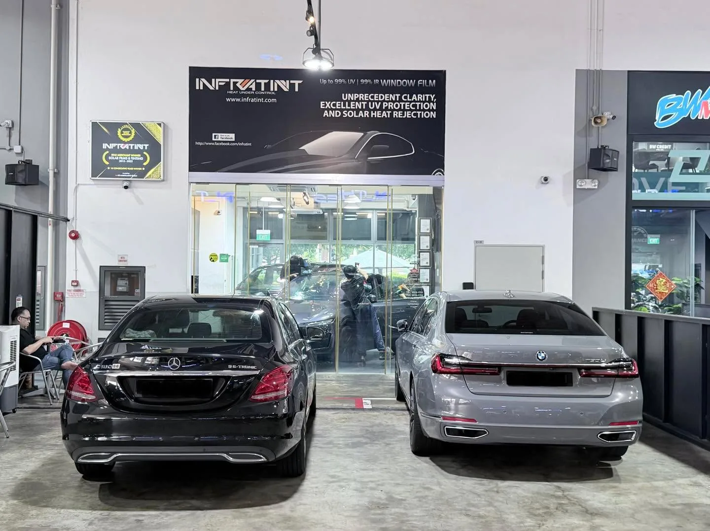 A black Mercedes-Benz sedan and white BMW sedan facing the camera in the workshop.