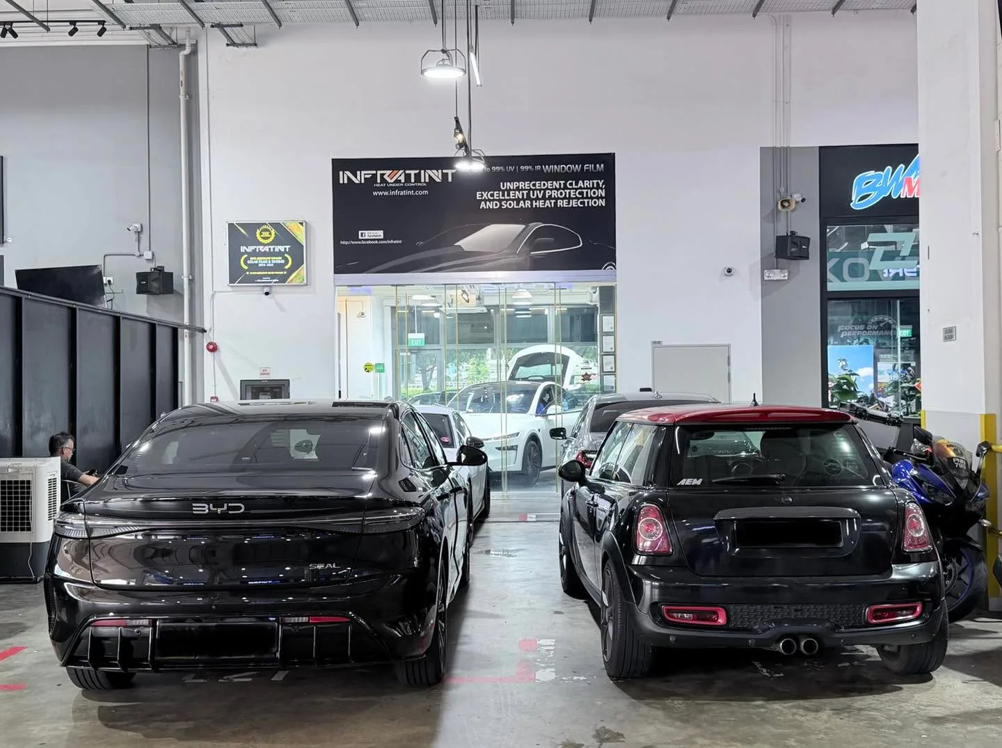 A black BYD sedan and white Tesla Model Y in the workshop.